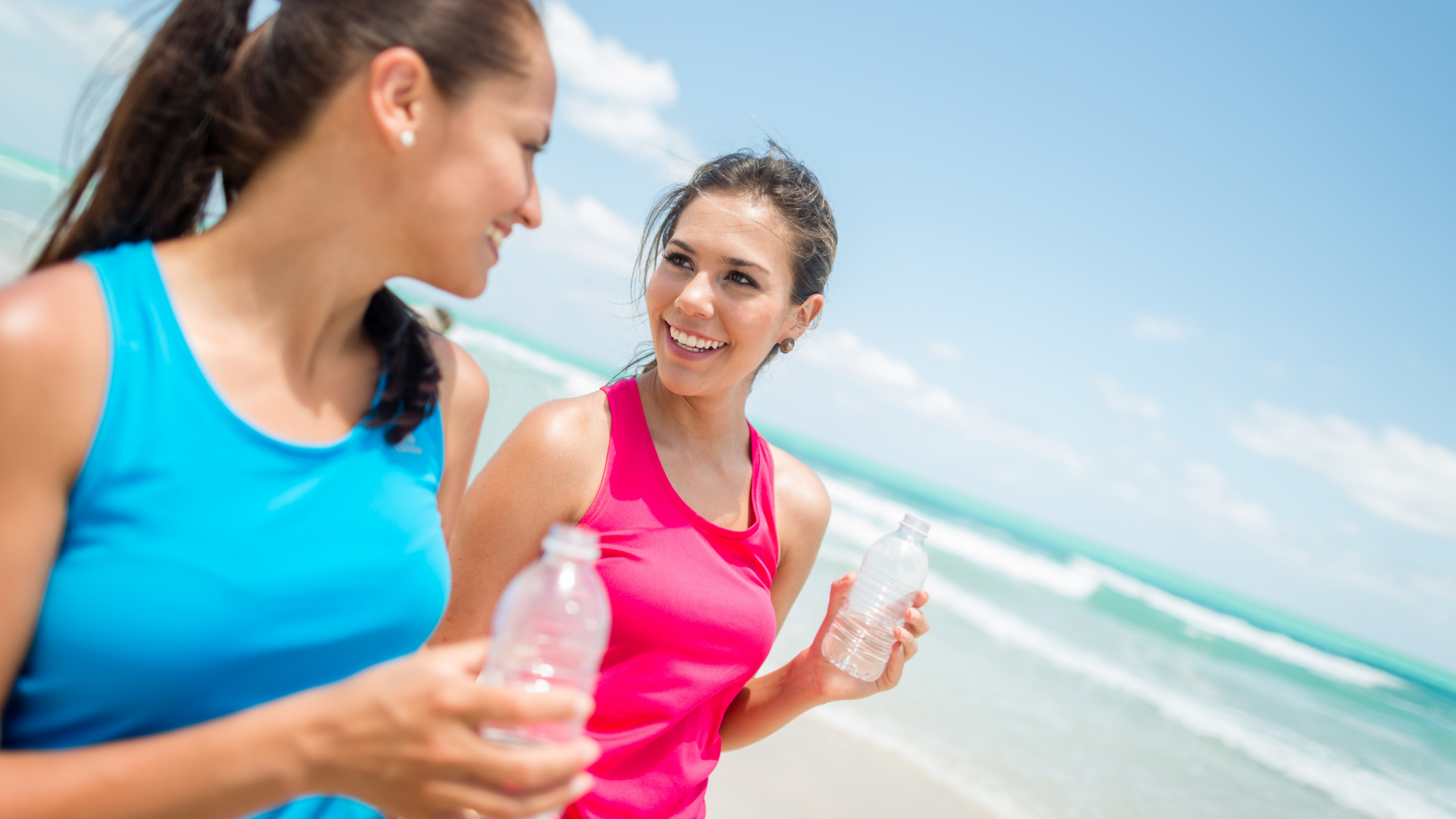 two women drinking from water bottles and running on the beach